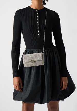 Abito lungo a maniche lunghe nero a coste con scollatura a henley e bottoni metallici; abbinato a una borsa a tracolla metallica argento decorata con strass.