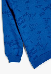 Blaues Sweatshirt aus strukturiertem Stoff, mit grafischen Mustern und bedrucktem Text, der "FOLLOW ME BACK" umfasst, sowie gerippten Bündchen für eine taillierte Optik.