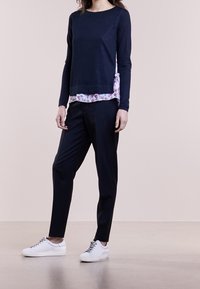 Marinblå långärmad topp med blommig sidopanel, kombinerad med svarta byxor och vita sneakers. Slät textur, avslappnad design.