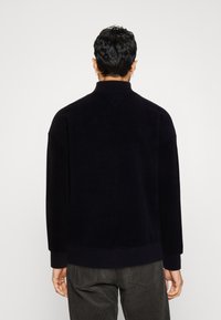 Czarna, teksturowana bluza z polaru z wysokim kołnierzem i ściągaczami na rękawach. Charakteryzuje się luźnym krojem oraz minimalistycznym designem bez widocznych logo.