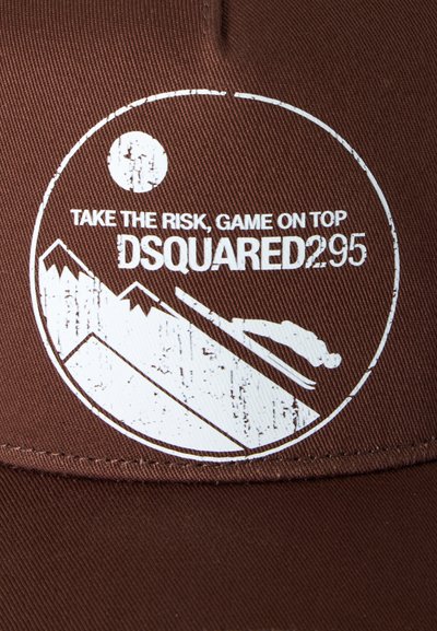 Tela marrón con un diseño circular blanco que muestra montañas, un esquiador y el texto "Take the risk, game on top DSQUARED2 95".