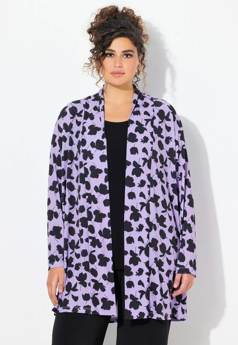 Violetti neuletakki, jossa on musta kukkakuosi, pitkät hihat ja avoin etuosa. Puettu mustan paidan päälle. Pehmeä kangas.