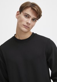 Black sweatshirt with a crew neckline, soft fabric, relaxed fit, and minimal stitching details. Texture appears smooth and matte.