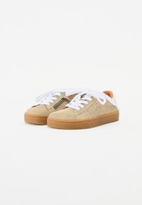 Bež nubukist sneakerid valgete paeltega, ümar varvas, külgedel perforatsioonid ning heleroheline kummitald. Tõmbluku detail välisküljel.