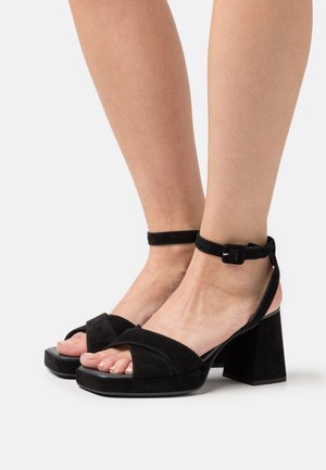 Sandales à talons blocs en daim noir avec une lanière à la cheville, bout ouvert et design croisé à l'avant. Texture lisse et construction robuste.