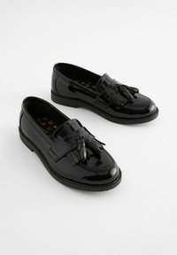 Loafers din piele patentă neagră, cu vârful rotund, detaliu de franjuri și ciucuri pe o talpă plată, având un grip texturat.