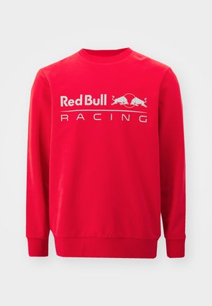 Sarkans garām piedurknēm izgatavots tīkla krekls no kokvilnas, ar apļa dekoltē. Izcili redzams ir "Red Bull Racing" logotips baltā krāsā.