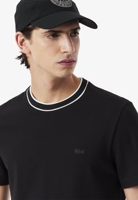 T-shirt nera a maniche corte realizzata in materiale testurizzato, con colletto doppio bianco e piccolo logo nero sul petto.