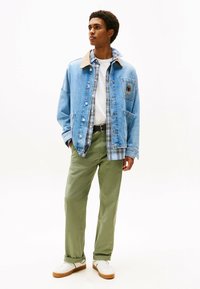 Giubbotto di jeans con colletto beige, camicia a quadri sotto, t-shirt bianca, pantaloni verde oliva e sneakers bianche con suola in legno.