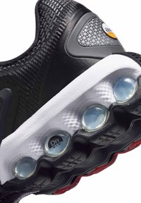 Black athletic shoe with textured upper, visible air cushioning pods, and rubber outsole with red accents and logo detail.