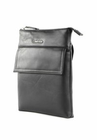 Sacoche pour tablette en cuir noir avec fermeture éclair, poche avant et logo Calvin Klein. Présente une texture lisse et une forme rectangulaire élégante.