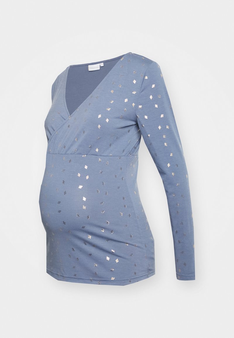 Blusa de maternidade de manga longa azul com decote em V, apresentando padrões quadrados metálicos prateados e um design ajustado que acomoda uma barriga em crescimento.