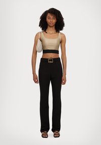 Crop top in raso dorato con elastico nero. Pantaloni neri sartoriali con fibbia dorata. Borsa a rete argentata e sandali neri con cinturini.