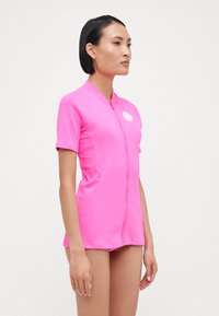 Pink short-sleeve swimsuit with ribbed texture, front zipper, and a round logo. Fitted style with a high neck.