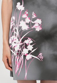 Grijs satijnen jurk met een roze en witte bloemenprint, met delicate stelen en bloemblaadjes. De stof heeft een gladde, glanzende textuur.