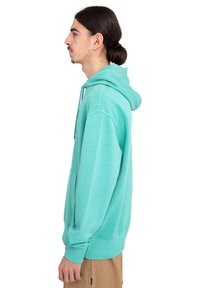 Sudadera turquesa hecha de una tela suave, con un bolsillo frontal y capucha ajustable. El diseño es de corte relajado con puños y dobladillo acanalados.