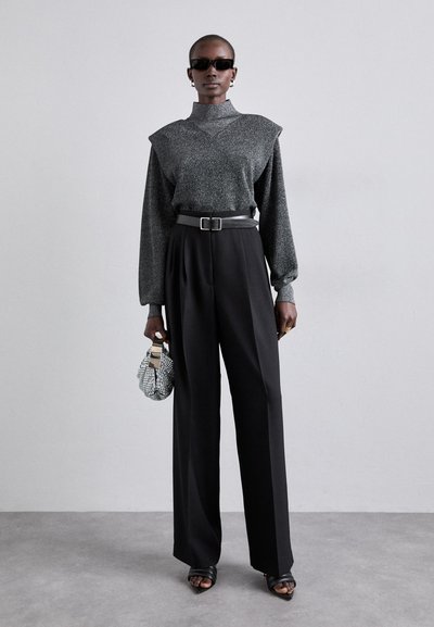 Top de manga larga texturizado en gris con adornos en los hombros, combinado con pantalones negros de cintura alta. Los accesorios incluyen un cinturón metálico y un bolso pequeño.