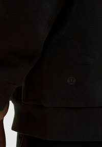 Czarny sweatshirt z teksturowanej tkaniny, z prążkowanymi mankietami i dołem; posiada małe, okrągłe logo na dolnej lewej stronie.