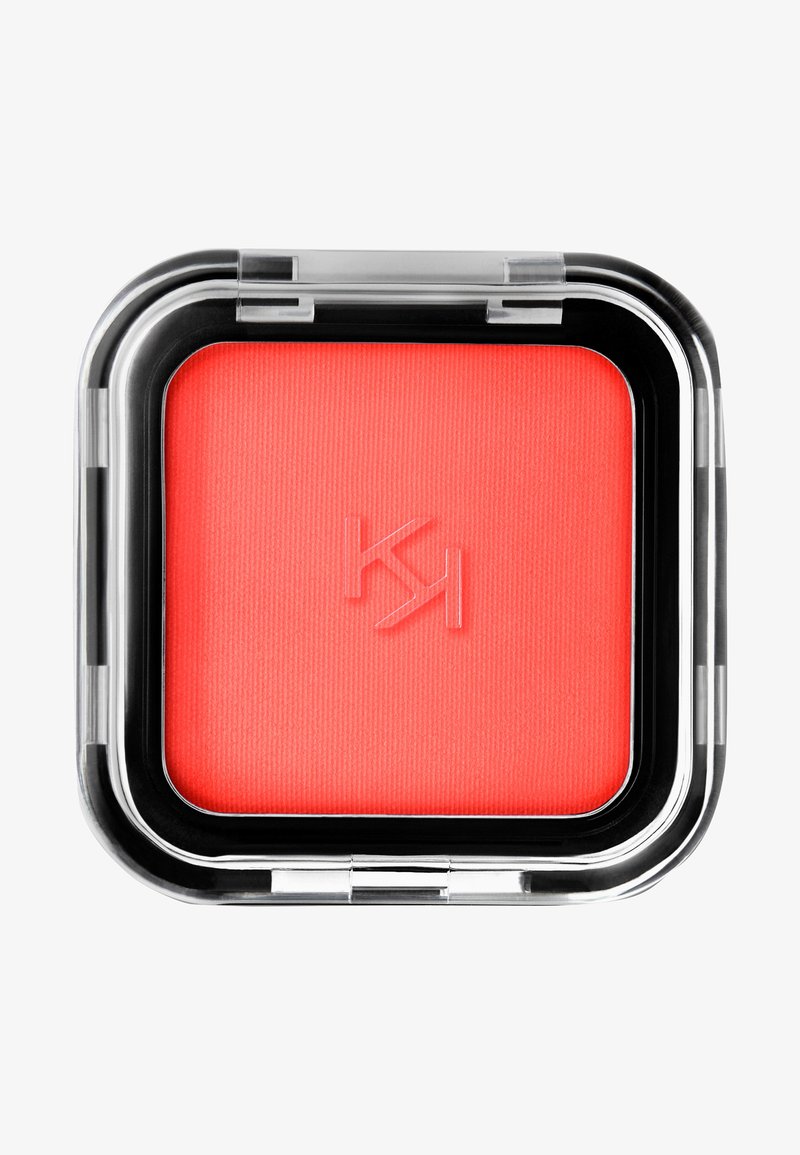 Koraalroze blush in een vierkante zwarte en doorzichtige compact. Geribbelde textuur op het oppervlak, logo in de blush gedrukt, gladde randen op de verpakking.
