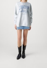 Sudadera gris con gráfico de "LONDRES" en azul, combinada con una mini falda de mezclilla y botas negras de tacón alto. Conjunto informal con texturas mixtas.