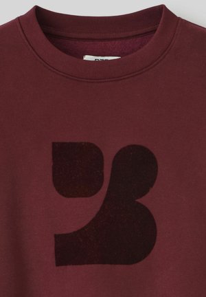 Sweatshirt bordeaux avec un grand motif graphique noir semi-transparent au centre. Col rond côtelé et texture douce.