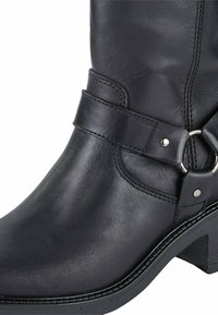 Schwarze Leder-Ankle Boots mit abgerundeter Zehenform, dekorativem Riemen, metallischem Ringakzent und niedrigem, gestapeltem Absatz. Glatte Textur und polierte Oberfläche.