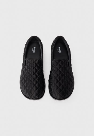 Svarta vadderade slip-on skor med en slät yta, rund tå och vadderad krage. Insidan har en logotyp. Enkelt design utan synlig hårdvara.