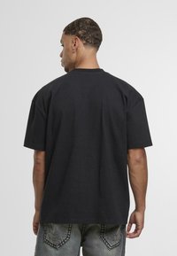 Camiseta de algodón negra con un corte relajado, mangas cortas y un escote redondo. Detalles de costura visibles y sin gráficos en la parte trasera.