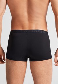 Svarta boxerkalsonger i mjukt tyg med en logoband. Designen är åtsittande och slät, med en sömlös utseende.