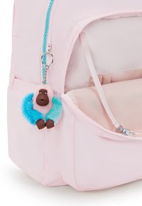 Růžový batoh vyrobený z látky, s tyrkysovým zipem. Na stříbrném klíčence visí barevný přívěsek opičky s růžovým a modrým kožíškem.