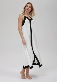Witte jurk met zwarte accenten, met een diepe V-hals, verstelbare bandjes en een losse, vloeiende stijl. Getextureerde stof, kuitlang.