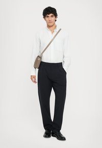 Weiß gestreiftes Langarmhemd, schwarze Hose, schwarze Schuhe und eine hellbraune Umhängetasche. Einfaches Design und taillierte Passform.