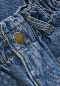 Denimtyg i ljusblått med en texturerad yta. Har en elastisk midja med samlat material och en bronstonad knappdetalj.