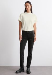 Lichtbeige shirt met korte mouwen en hoge hals, gecombineerd met zwarte slim-fit jeans. Zwarte instappers maken de outfit compleet. Eenvoudig ontwerp, zachte textuur.