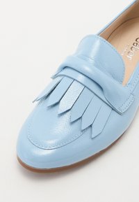 Light blue leather loafer with fringe detailing, rounded toe, and a smooth, glossy finish. The sole is flat and brown.