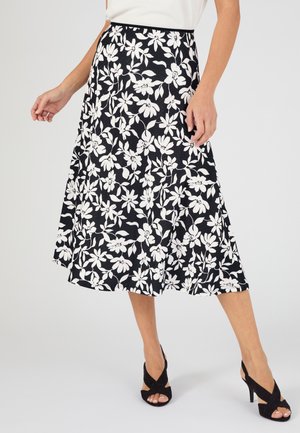 Falda midi negra con estampado floral blanco, combinada con tacones negros abiertos en los dedos y una blusa blanca, vista desde la cintura hasta la mitad de la pantorrilla.