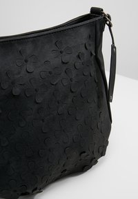 Bolso de mano negro con un patrón de flores en relieve, hecho de material texturizado, cuenta con una correa para el hombro y una abertura en la parte superior.