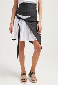 Svart randig kjol med vit veckad underkjol, med en midjeband och en ficka, kompletterad med svarta och silverfärgade sandaler.