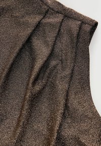 Fémes bronz szövet, texturált felülettel, redőkkel a nyakvonal mentén. Az anyag csillogó, szőtt megjelenésű.