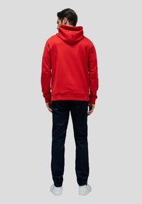 Sudadera roja con una capucha espaciosa, puños y dobladillo acanalados, combinada con pantalones azul marino. El conjunto incluye zapatillas blancas. Se muestra la vista posterior.