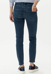 Jean skinny bleu foncé avec une texture lisse, poches arrière et détails de coutures subtils, associés à des baskets blanches et marine.