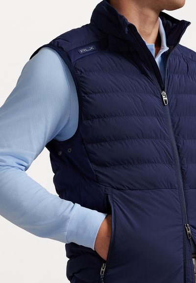 Navy puffer vest with high collar, zip closure, and RLX logo. Features a quilted design and side pockets; paired with a light blue long-sleeve shirt.