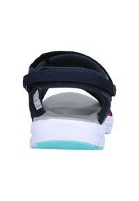 Tumman sininen sandaali säädettävillä kankaasta valmistetuilla remmeillä, valkoisella pehmustetulla pohjalla ja teallla varustetulla ulkopohjalla. Varustettu sileällä sisäpohjalla.