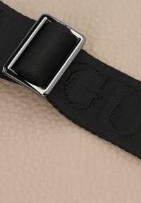 Cintura in tessuto nero con testo impresso, fissata da una lucida fibbia metallica rettangolare, su uno sfondo beige testurizzato.