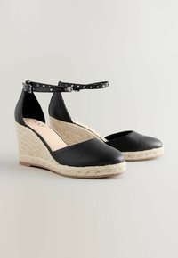 Čierne wedge espadrilky s textúrovaným koženým zvrškom, platformou obalenou jútou, remienkom okolo členku s striebornými cvočkami a zaobleným prstom.