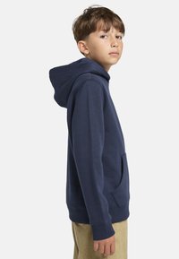 Námornícky modrá mikina s kapucňou vyrobená z mäkkej tkaniny, s prednou kapsou, rebrovanými manžetami a kapucňou so sťahovacou šnúrkou. Minimalistický dizajn.