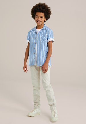 Camicia a maniche corte, a righe blu e bianche, con taschino sul petto, abbinata a pantaloni chiari e sneaker bianche.