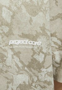 Šviesiai smėlinė marškinėlių su tekstūruotu, abstrakčiu raštu. Yra baltas logotipas "project core" ir detalė "THE CORE UNLIMITED EDITION".
