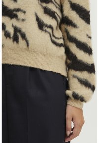 Beige trui met zwarte tijgerstrepen, gemaakt van een fluffy materiaal. Heeft ribgebreide manchetten en zoom, gecombineerd met donkere, gestructureerde broek.
