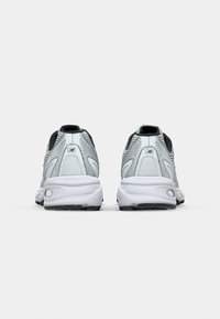 Paire de chaussures de course New Balance blanches et grises vues de dos sur un fond gris clair uni.